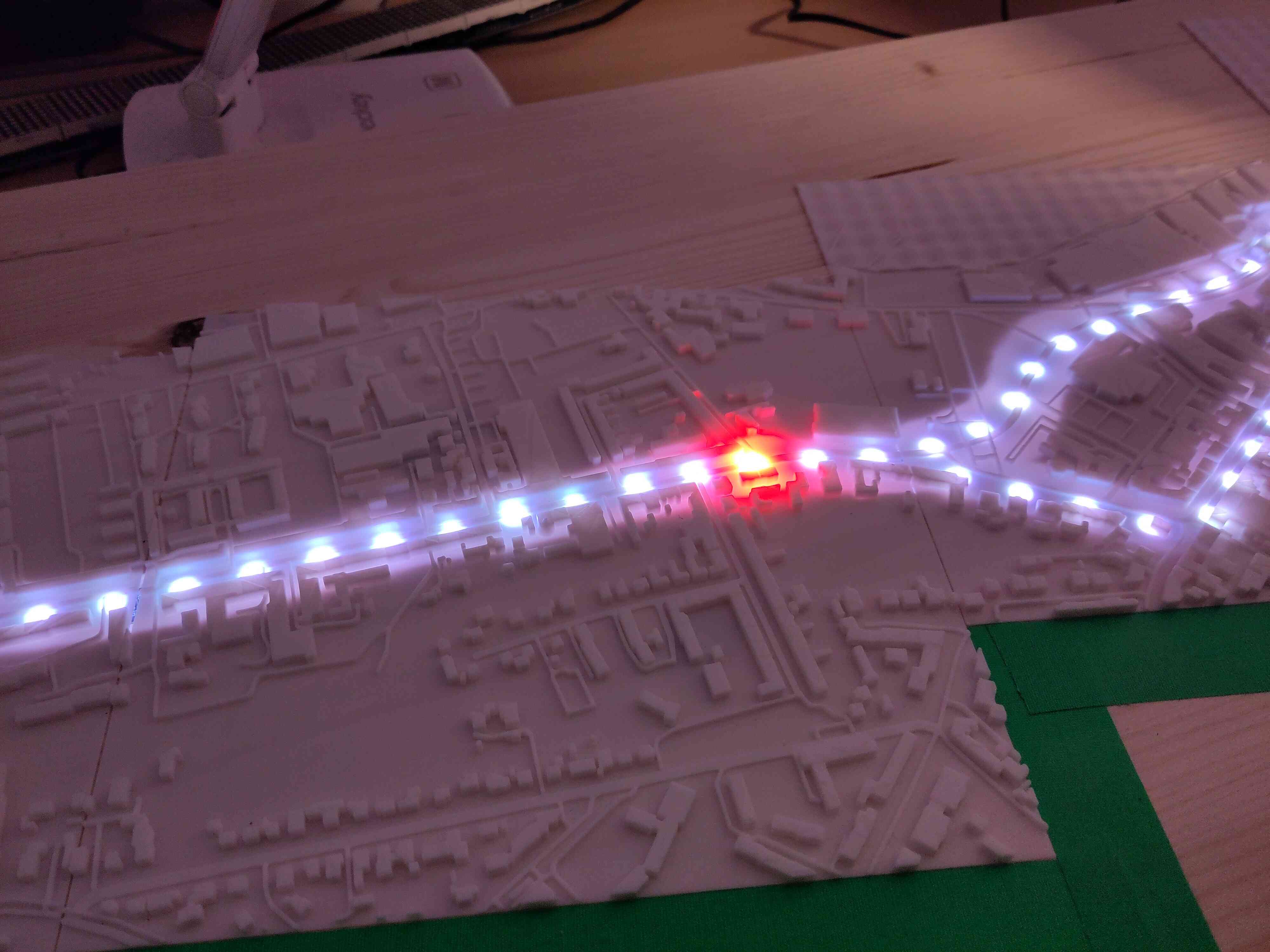 Auf einer 3D gedruckten Stadtkarte ist im Hintergrubd durchzusehen das auf der einen Linie weiße LEDs durchleuchten und ein sich eine einzelne rote bewegt