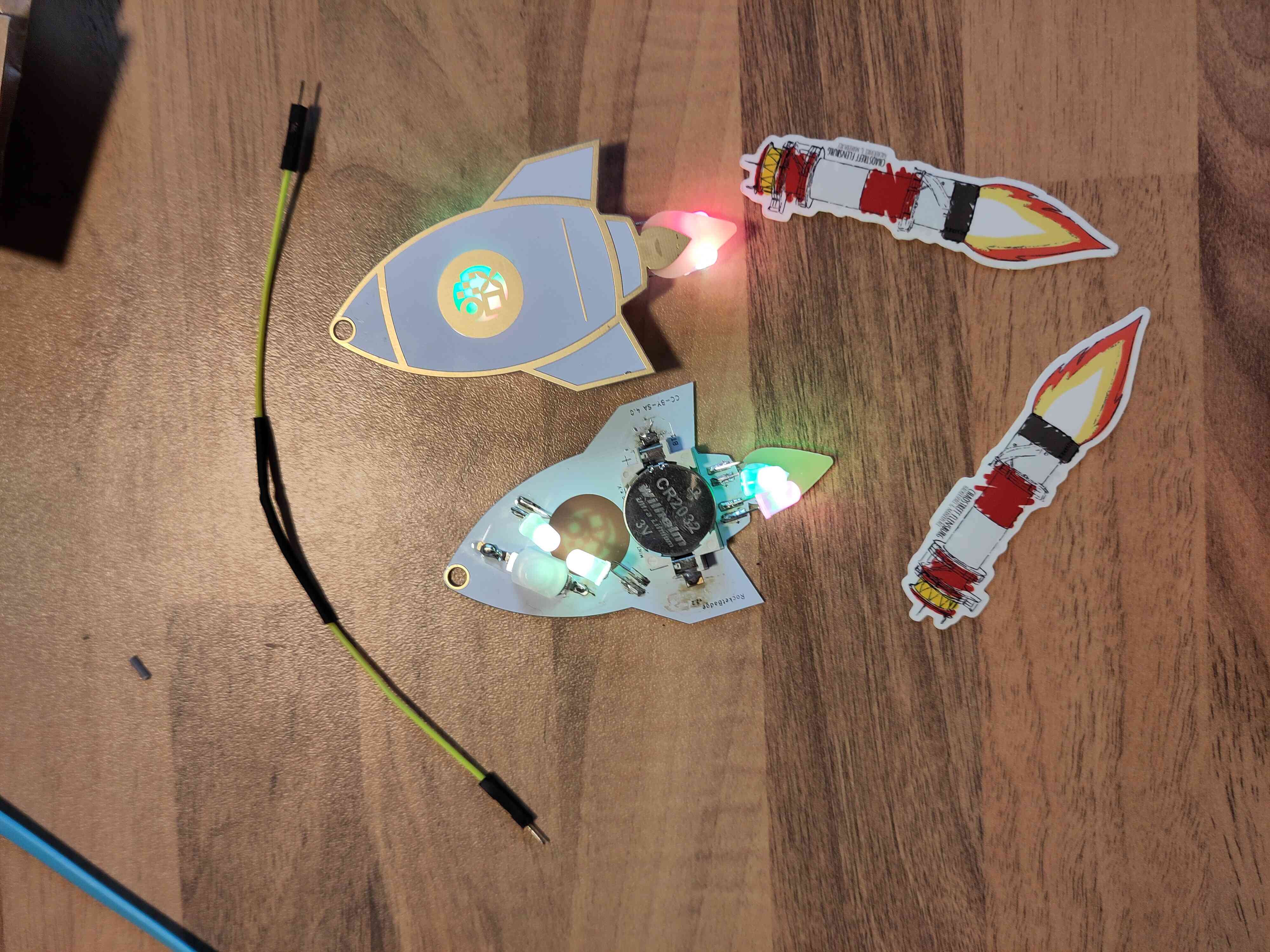 Ein Kabel mit schrumpfschlauch. Zwei Raketen mit leuchtenden LEDs die gelötet sind und zwei Leuchtturm rakeden Sticker vom ctfl